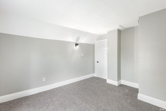 empty room featuring dark carpet, vaulted ceiling, and baseboards