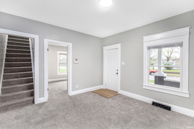 foyer entrance featuring baseboards, visible vents, carpet floors, and stairway