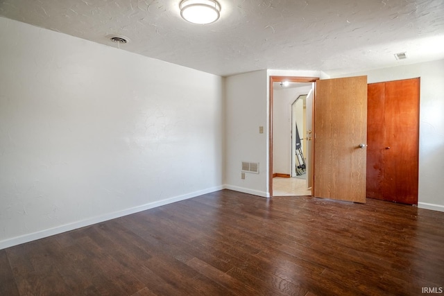 unfurnished room with wood finished floors, visible vents, a textured ceiling, and baseboards