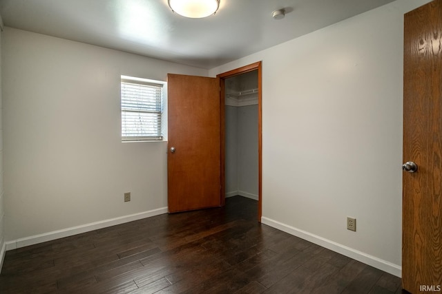 unfurnished bedroom with a closet, dark wood finished floors, and baseboards