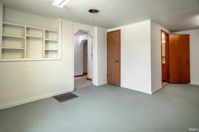 spare room with concrete floors, baseboards, and arched walkways