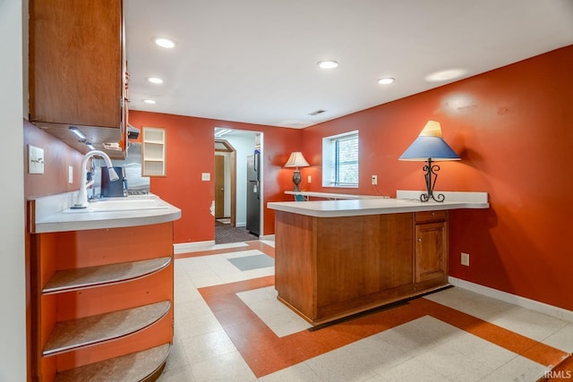 kitchen with baseboards, a peninsula, brown cabinetry, and light countertops