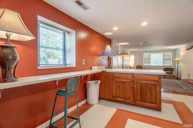kitchen featuring a wealth of natural light, a peninsula, brown cabinetry, and light countertops