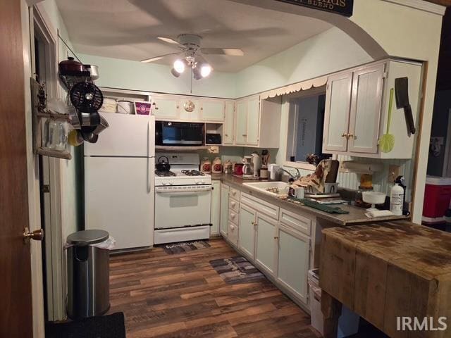 kitchen with white appliances, dark countertops, dark wood-style flooring, a sink, and a ceiling fan