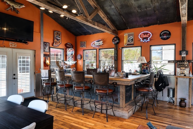 bar with beamed ceiling, a bar, wood-type flooring, high vaulted ceiling, and french doors