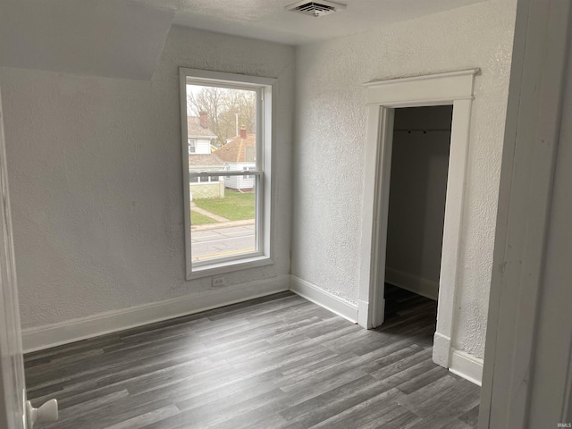 unfurnished bedroom featuring wood finished floors, a textured wall, visible vents, and baseboards