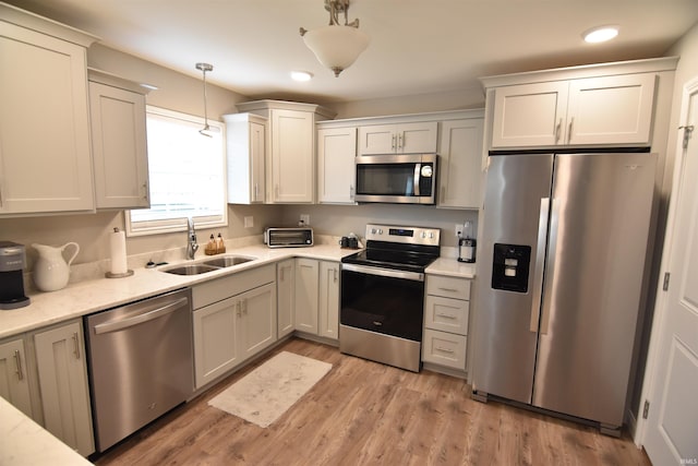 kitchen featuring recessed lighting, decorative light fixtures, appliances with stainless steel finishes, a sink, and light wood-type flooring