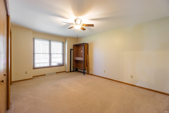 unfurnished room featuring light colored carpet, visible vents, a ceiling fan, and baseboards