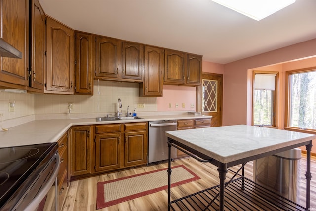 kitchen featuring light wood-style flooring, decorative backsplash, brown cabinetry, appliances with stainless steel finishes, and a sink