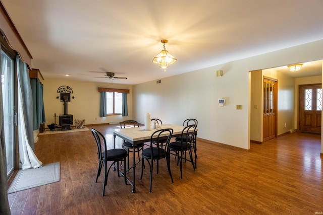 dining room featuring visible vents, a wood stove, wood finished floors, and baseboards
