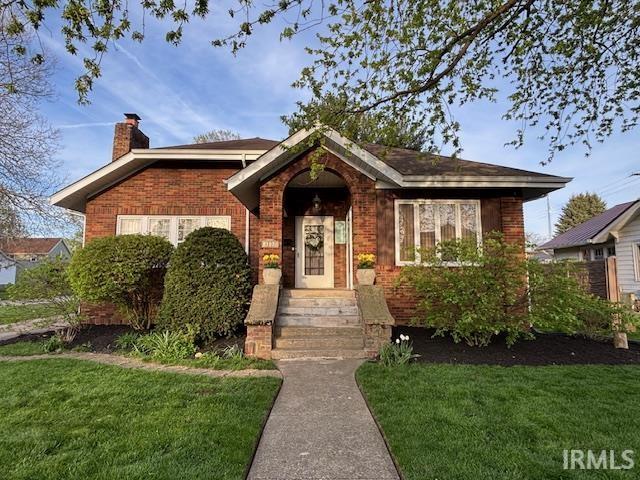 view of front of house featuring a chimney, a front yard, and brick siding