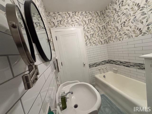 full bathroom with a bathing tub, tile walls, wallpapered walls, and a sink
