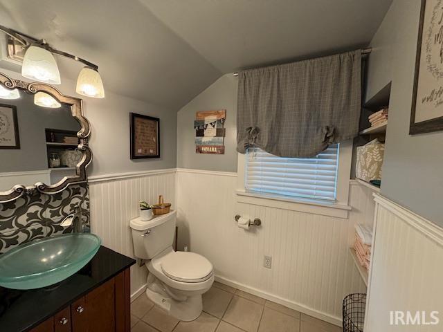 bathroom with vanity, toilet, tile patterned flooring, wainscoting, and lofted ceiling