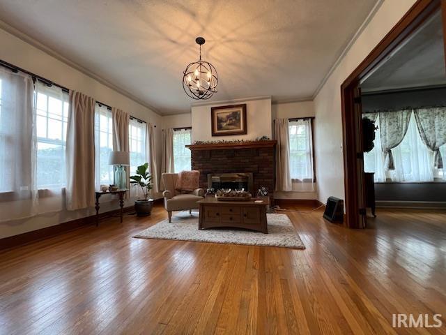 living area featuring hardwood / wood-style flooring, a chandelier, crown molding, and a brick fireplace