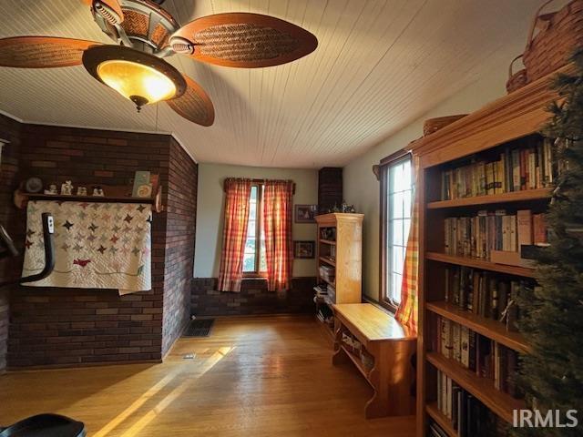 interior space featuring a wealth of natural light, wood finished floors, ceiling fan, and brick wall