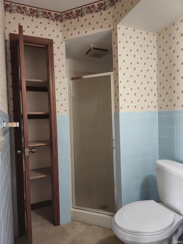 bathroom with a shower stall, wallpapered walls, toilet, tile walls, and wainscoting