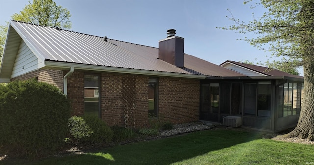 back of property with a lawn, a sunroom, a chimney, and brick siding