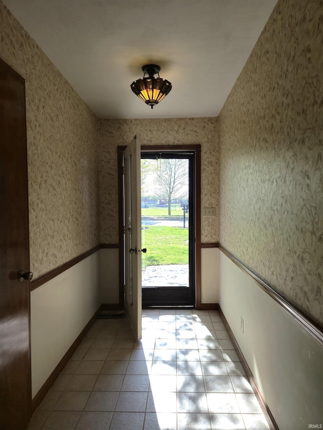 doorway with light tile patterned floors, wallpapered walls, and baseboards