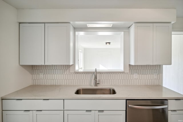 kitchen featuring stainless steel dishwasher, a sink, white cabinets, and tasteful backsplash