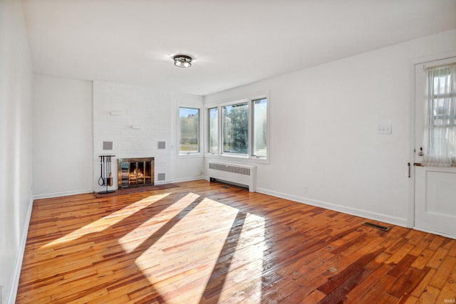 unfurnished living room with hardwood / wood-style flooring, radiator heating unit, a fireplace, baseboards, and visible vents