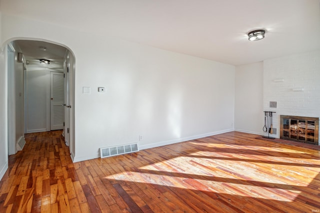unfurnished living room with a fireplace, wood-type flooring, visible vents, baseboards, and arched walkways
