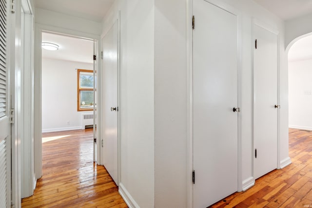 hallway featuring baseboards, arched walkways, radiator heating unit, and light wood-style floors