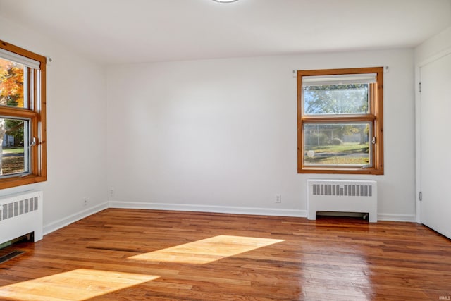 unfurnished room featuring baseboards, radiator heating unit, and wood finished floors