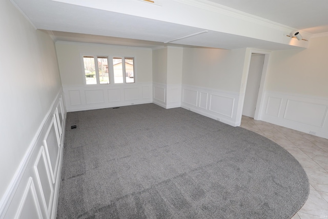 empty room featuring light colored carpet, a decorative wall, ornamental molding, and wainscoting