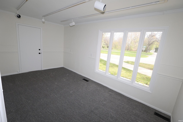 empty room with track lighting, visible vents, ornamental molding, and dark carpet