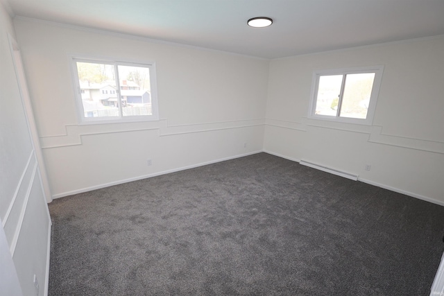 spare room with dark colored carpet, a healthy amount of sunlight, ornamental molding, and a baseboard heating unit