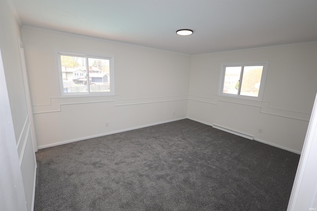 unfurnished room with dark carpet, a baseboard heating unit, ornamental molding, and plenty of natural light
