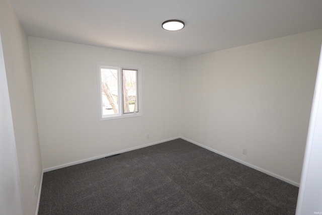 unfurnished room with visible vents, dark colored carpet, and baseboards