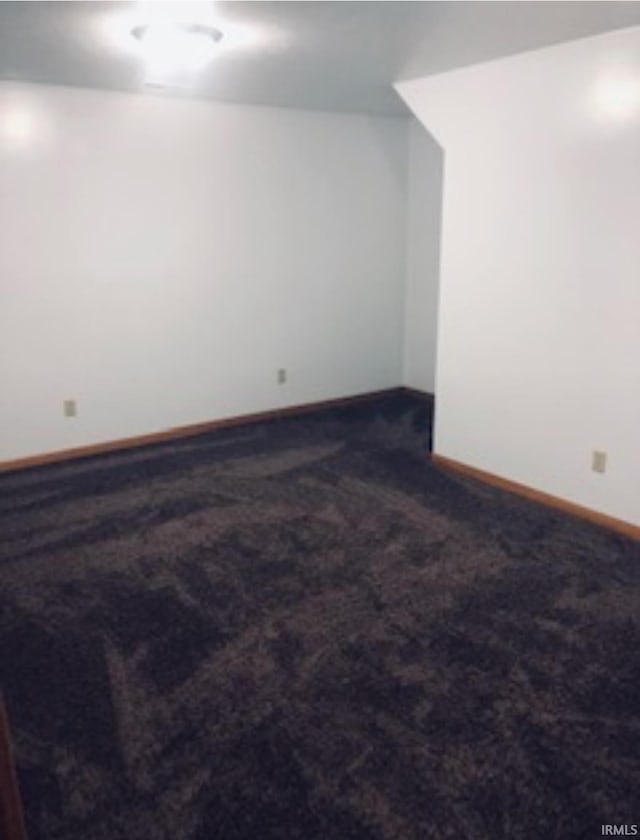additional living space featuring baseboards and dark carpet