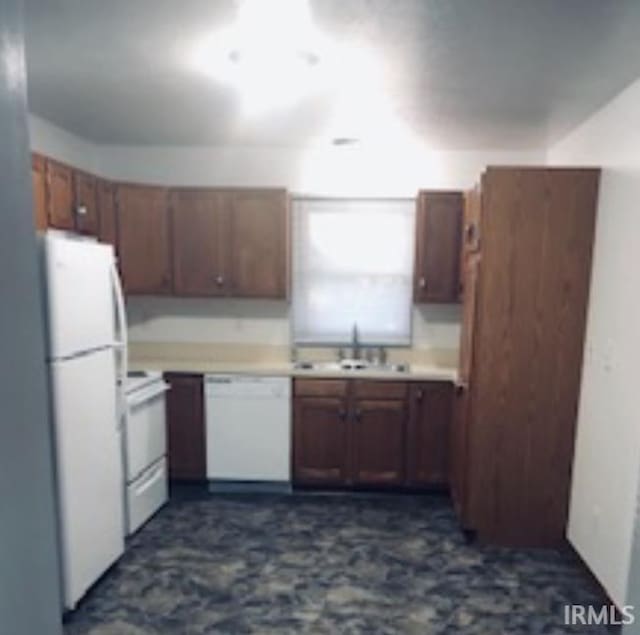kitchen with brown cabinetry, a sink, white appliances, and light countertops