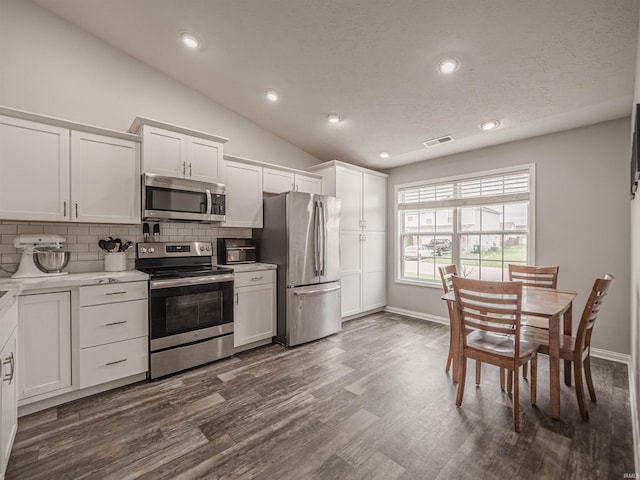 kitchen with white cabinetry, tasteful backsplash, appliances with stainless steel finishes, vaulted ceiling, and dark wood finished floors