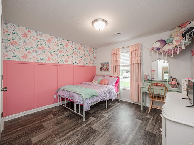 bedroom with visible vents, wallpapered walls, wood finished floors, and wainscoting