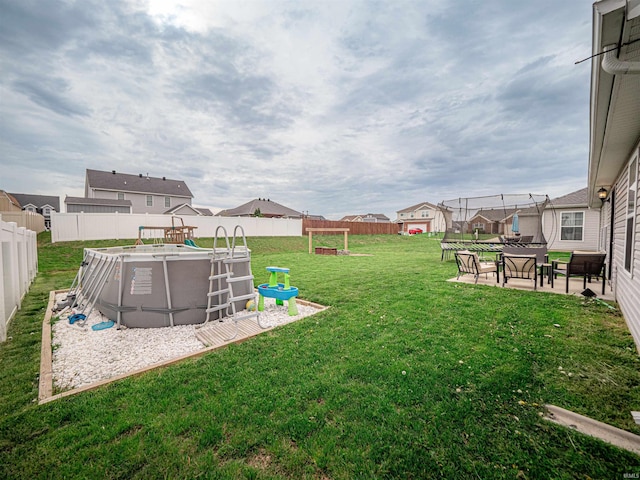 view of yard featuring a trampoline, a fenced backyard, a fenced in pool, a residential view, and a patio area