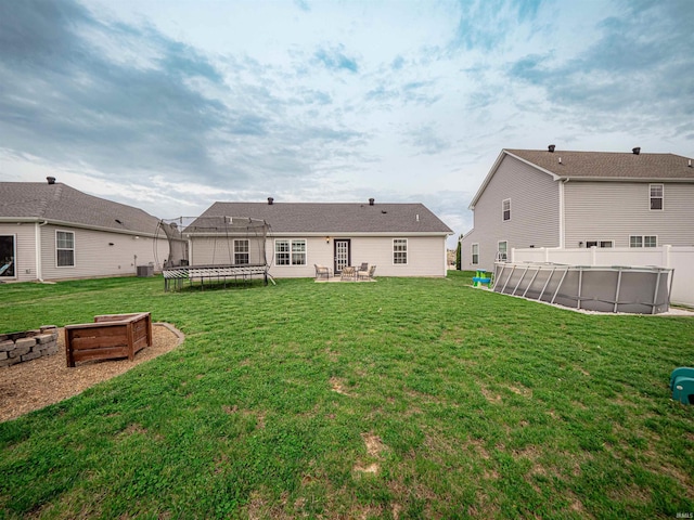 rear view of house with a trampoline, an outdoor fire pit, a patio area, a fenced in pool, and a lawn