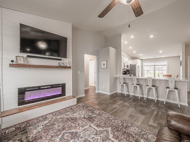 living room with ceiling fan, a large fireplace, baseboards, dark wood-style flooring, and vaulted ceiling