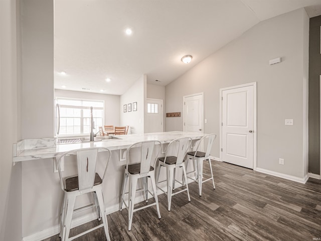 kitchen with recessed lighting, a kitchen bar, vaulted ceiling, baseboards, and dark wood finished floors