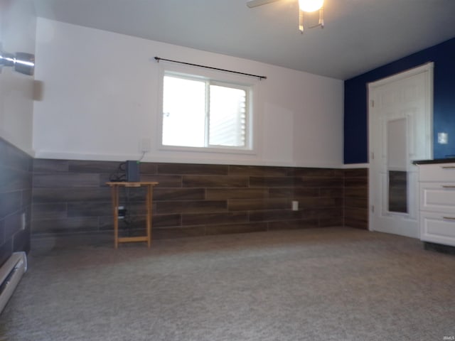 unfurnished living room featuring carpet, a ceiling fan, a wainscoted wall, and baseboard heating