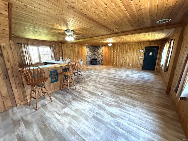 dining space featuring a ceiling fan, a stone fireplace, wood finished floors, wooden ceiling, and wooden walls