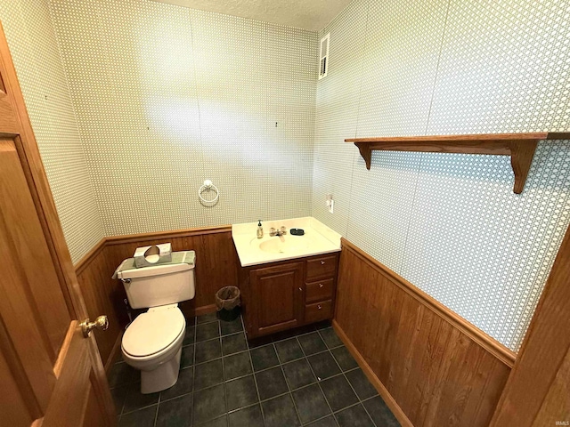 half bath featuring tile patterned flooring, wainscoting, toilet, wooden walls, and wallpapered walls