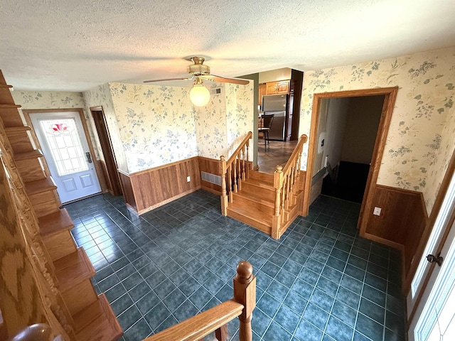foyer entrance featuring wallpapered walls, visible vents, ceiling fan, and a wainscoted wall