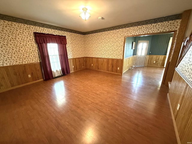 spare room featuring a wainscoted wall, baseboards, wallpapered walls, and wood finished floors