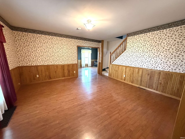 unfurnished room with stairs, wainscoting, wood finished floors, wooden walls, and wallpapered walls