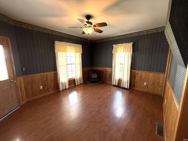spare room with a healthy amount of sunlight, wainscoting, a wood stove, and visible vents