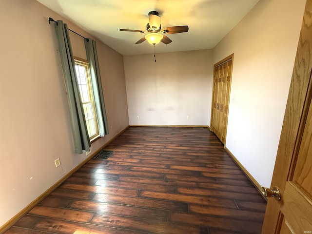empty room featuring visible vents, a ceiling fan, baseboards, and dark wood-style floors