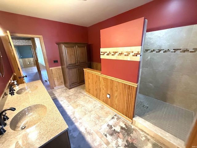 bathroom with double vanity, a sink, a walk in shower, and a wainscoted wall