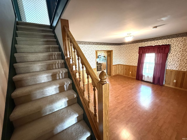 staircase with wood finished floors, baseboards, a wainscoted wall, and wallpapered walls
